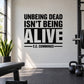 Black typography wall decal: 'UNBEING DEAD ISN'T BEING ALIVE' E.E. Cummings