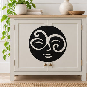 Swirl moon face decal: black circular stylized face with swirl eyes on light surface