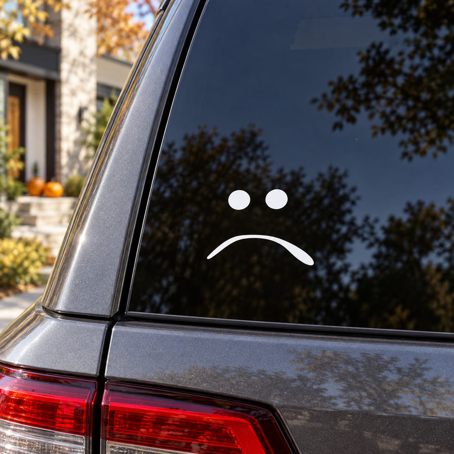 Frowning pumpkin face decal with two white dot eyes and arched frown on car window