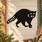 Black raccoon watching decal sticker with raised paw and tail on beige surface
