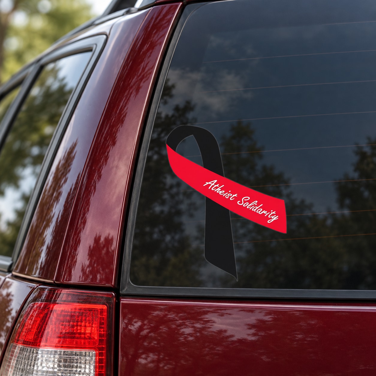 Vinyl awareness sticker: black ribbon with red banner and white cursive “Atheist Solidarity”