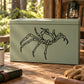 Crab spider decal, black line-art spider on light green surface.