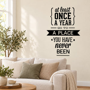 Black typography wall decal: 'At least once a year, go to a place you have never been'.