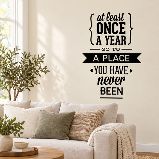 Black typography wall decal: 'At least once a year, go to a place you have never been'.