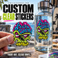 Clear vinyl custom sticker with colorful monster skull graphic, held near a water bottle