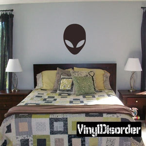 Alien face decal with dark oval head and light curved eyes on a wall