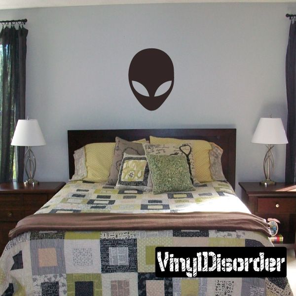 Alien face decal with dark oval head and light curved eyes on a wall