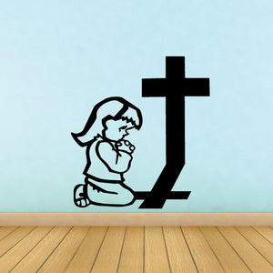 Cartoon girl praying decal with kneeling girl beside a cross, black line art.