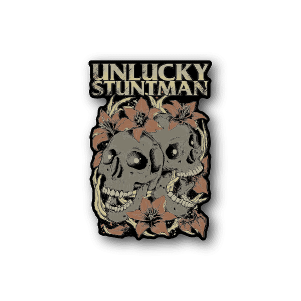 Vinyl sticker with Unlucky Stuntman text, twin skulls and leaves, tan.