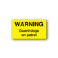 Yellow warning sticker, rectangular, black text: WARNING, Guard dogs on patrol.