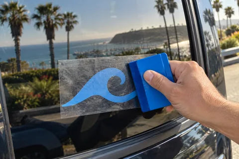 Illustrative coastal installation example: a squeegee smooths cut vinyl through its temporary transfer tape