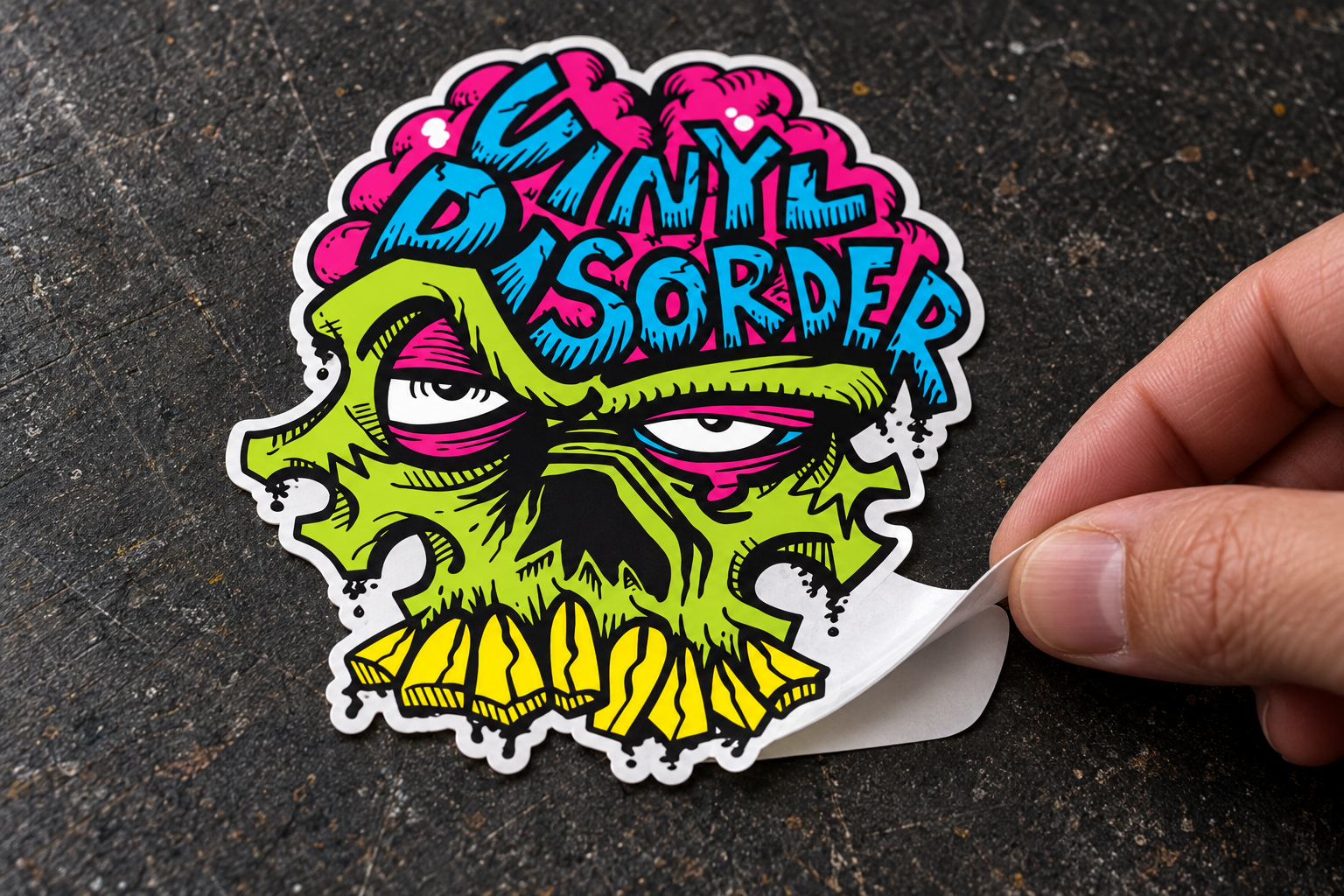 Illustrative close-up of the Vinyl Disorder skull sticker: a hand lifts its lower-right printed edge from an intact white backing.