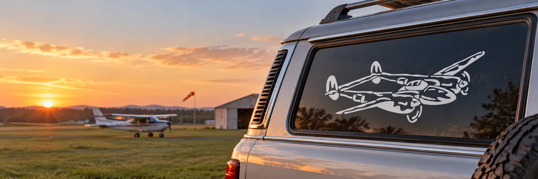 Illustrative Airplane Decals application scene: Rear quarter glass of a silver vintage SUV parked at a rural grass airstrip, exact reference P-38 aircraft graphic in white vinyl on dark window, small real light aircraft and sunset runway beyond. Natural diagonal camera angle, foreground glass.