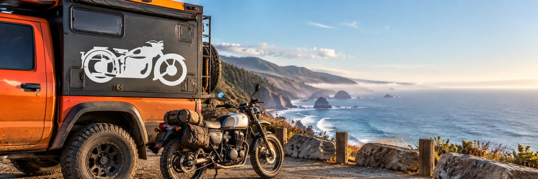 Illustrative Motorcycle Decals application scene: Coastal highway turnout with an orange adventure camper truck, exact reference motorcycle graphic in white vinyl on a dark smooth side panel, parked motorcycle and ocean cliffs. Wide cinematic road-trip story, cool ocean blue with orange vehicle.
